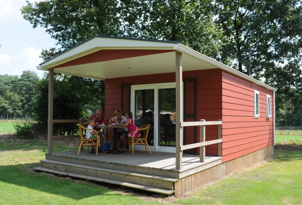 Een gezin zit op het terras van hun accommodatie een het bungalowpark op de Veluwe.